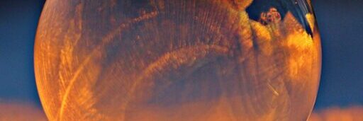 Close-up shot of a frozen bubble with warm reflections resting on a snowy surface at twilight.